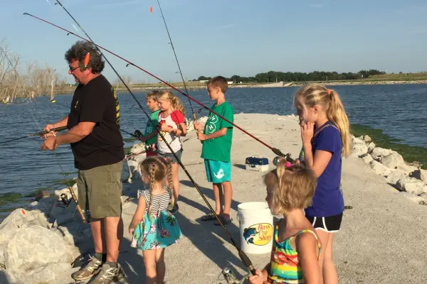 A group of kids and adults fishing on the beach.