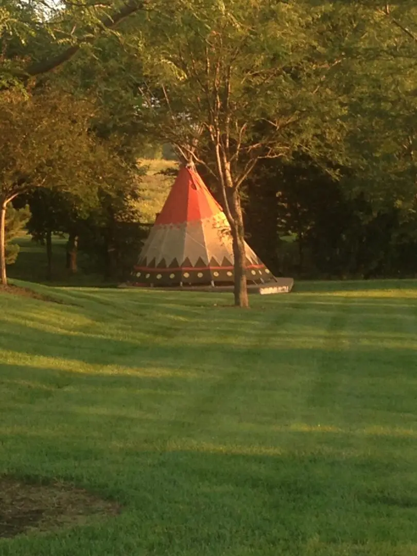 A red and white tipi in the middle of a field.