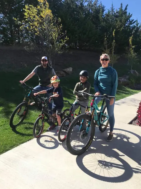 A family of four riding bikes on the sidewalk.