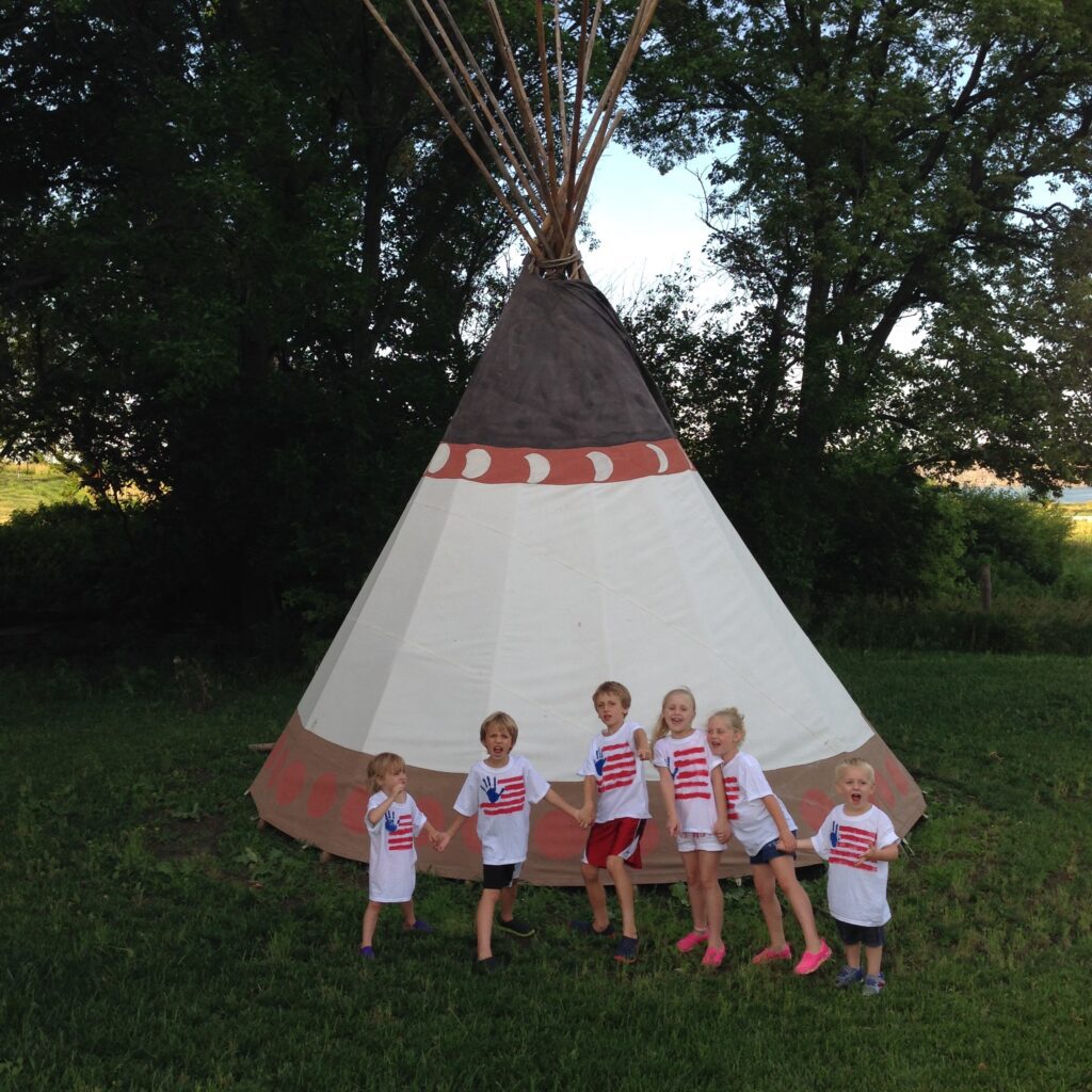 A group of children standing in front of a teepee.