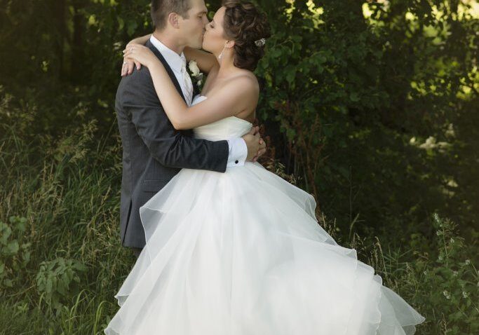 A man and woman kissing in front of trees.